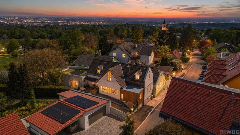 Abendliche Luftaufnahme der Wohnsiedlung mit Blick auf die beleuchtete Stadt in der Ferne.