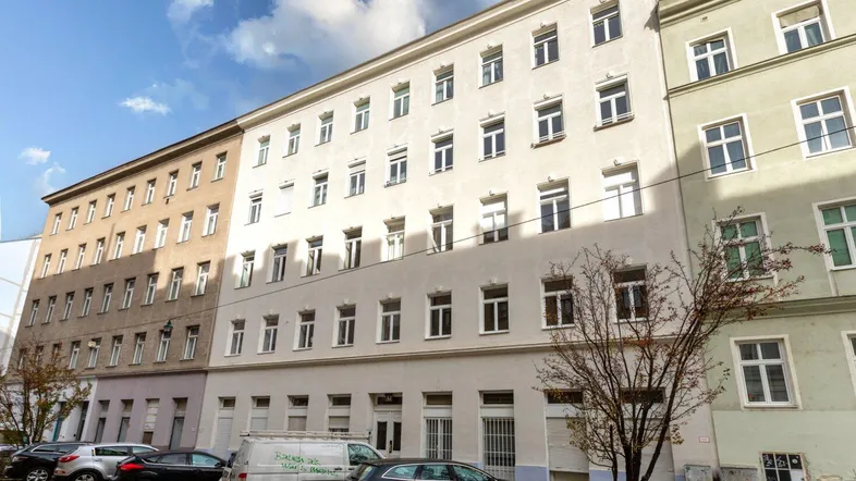 Mehrere Wohngebäude an einer Straße mit parkenden Autos unter blauem Himmel.