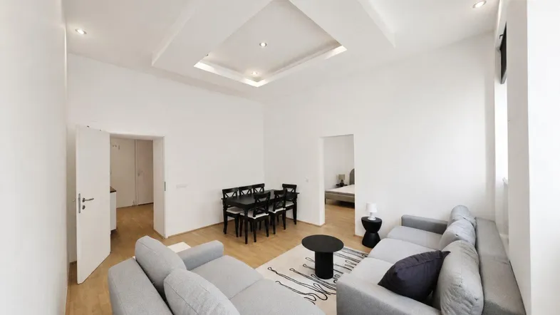 Heller Wohn- und Essbereich mit modernem Sofa, Esstisch und Holzboden, durch offene Türen sind weitere Räume sichtbar.