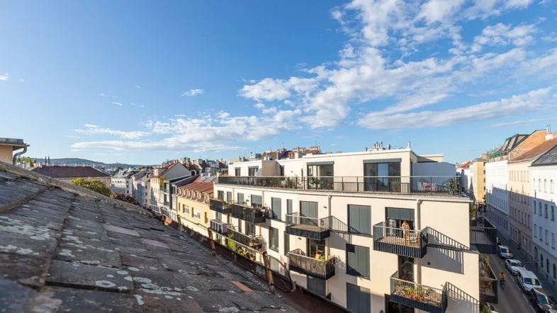 Blick über die Dächer der Stadt mit modernen Gebäuden und traditionellen Ziegeldächern unter blauem Himmel.