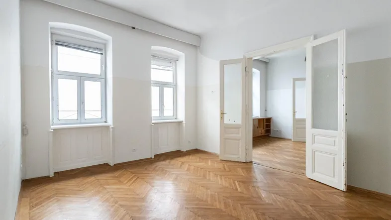 Helles Zimmer mit Fischgrätparkett und hohen Flügeltüren, das viel Potenzial bietet.