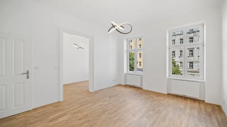 Geräumiges, helles Zimmer mit Parkettboden und Blick auf die umliegenden Gebäude.
