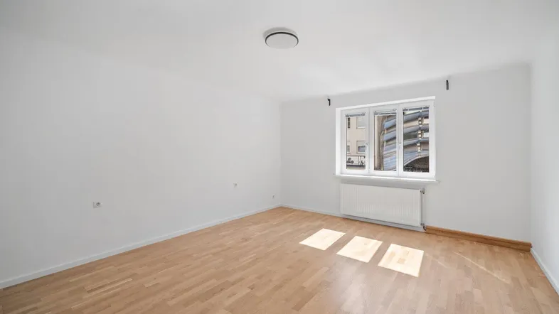 Helles, leeres Zimmer mit Parkettboden und weiß gestrichenen Wänden, ideal für individuelle Gestaltung.