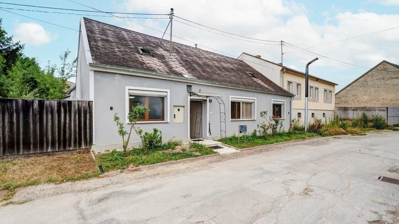 Einfamilienhaus mit grauer Fassade und dunklem Dach, gelegen an einer ruhigen Straße.