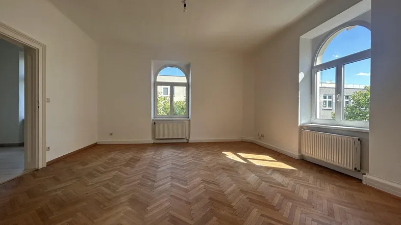 Helles Zimmer mit Fischgrätparkett und hohen Rundbogenfenstern, das viel Tageslicht hereinlässt.
