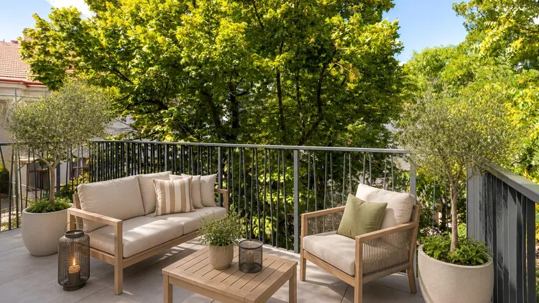 Möblierter Balkon mit bequemen Sitzgelegenheiten, Topfpflanzen und Blick ins Grüne an einem sonnigen Tag.