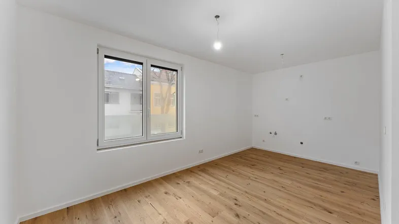 Helles, unmöbliertes Zimmer mit breitem Fenster, Holzboden und weißen Wänden.