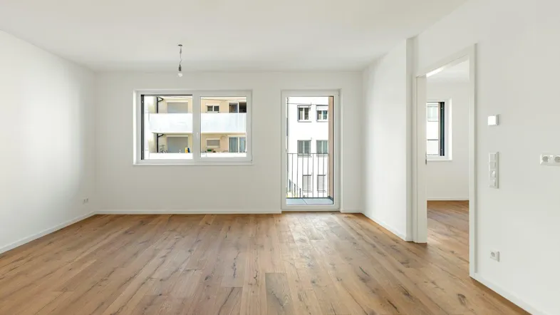 Helles, leeres Wohnzimmer mit Holzboden und Zugang zu einem französischen Balkon.