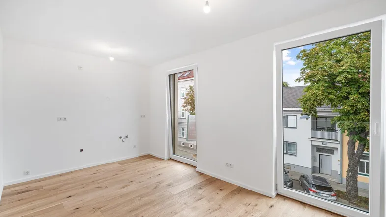 Helles Zimmer mit Holzboden und großen Fenstern, vorbereitet für eine moderne Kücheninstallation.