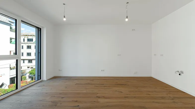 Helles, leeres Zimmer mit großen Fenstern und modernem Holzboden, bereit zur individuellen Gestaltung.