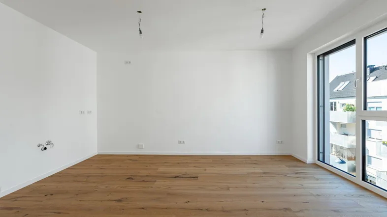 Helles, leeres Zimmer mit Holzboden und großen Fenstern, bereit für die Einrichtung.