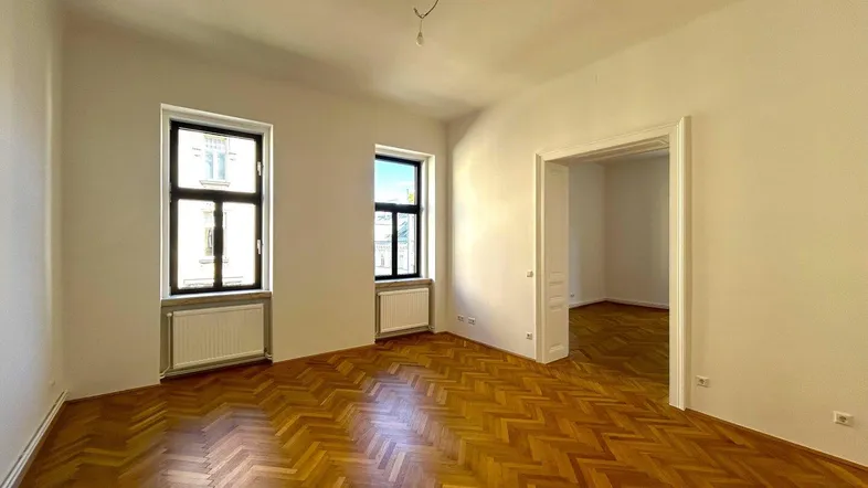 Helles Zimmer mit Fischgrätparkett, weißen Wänden und hohen Fenstern, bereit zum Einzug.