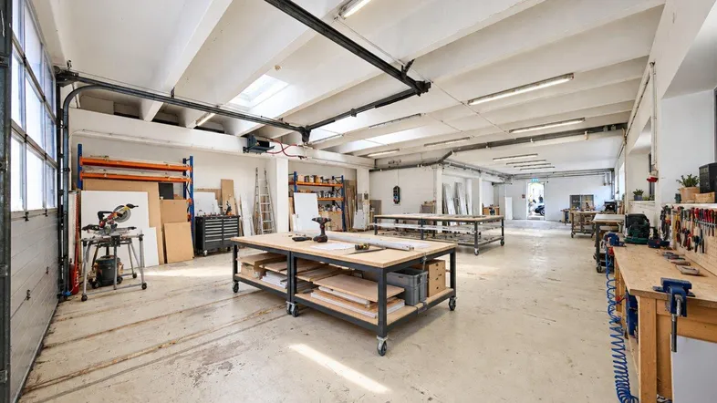 Geräumige Werkstatt oder Lagerhalle mit Betonboden, Rolltor und Arbeitsbereichen, ideal für handwerkliche Tätigkeiten.