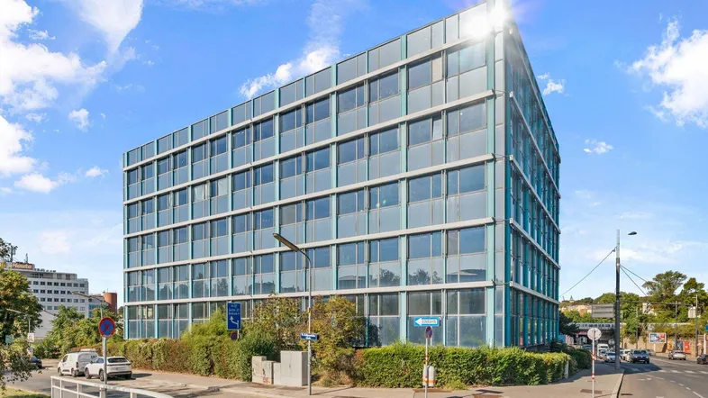 Modernes Bürogebäude mit Glasfassade und vielen Fenstern unter blauem Himmel.