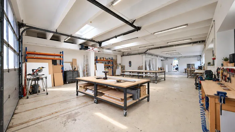 Geräumige Werkstatt mit hohen Decken, großen Fenstern und mehreren Arbeitsbereichen, ideal für handwerkliche Tätigkeiten.