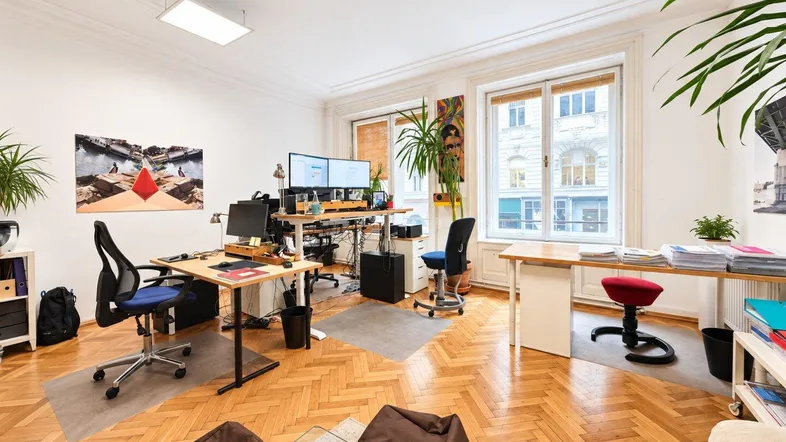 Geräumiges Büro mit mehreren Arbeitsplätzen, Parkettboden und großen Fenstern, die viel Tageslicht hereinlassen.