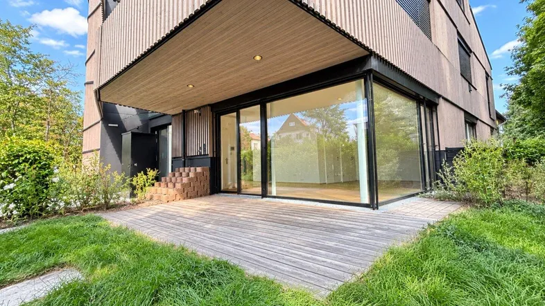 Moderne Gebäudefassade mit Holzverkleidung und einer großzügigen Holzterrasse im Erdgeschoss.
