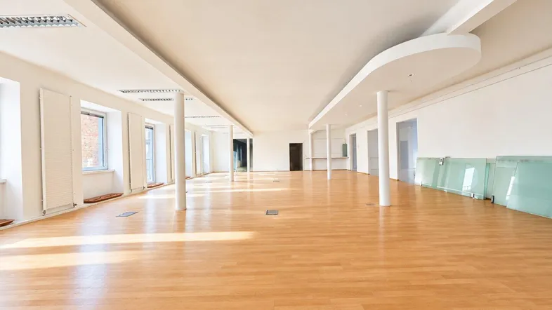 Großer, heller Büroraum mit Holzboden und vielen Fenstern, ideal für flexible Arbeitsplatzgestaltung.