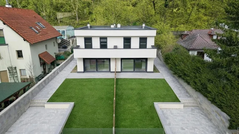 Moderne Doppelhaushälfte mit Flachdach, großzügiger Rasenfläche und Balkon, umgeben von viel Grün.