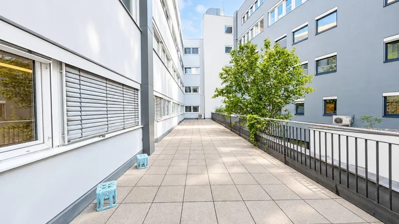 Geräumige Außenterrasse mit Fliesenboden zwischen zwei modernen Gebäuden, ideal für Pausen.