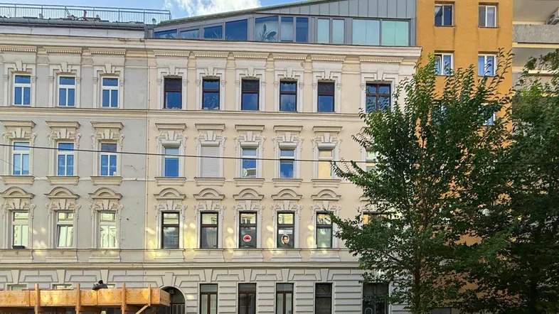 Fassade eines Mehrfamilienhauses mit klassischer Architektur und modernem Dachausbau unter blauem Himmel.