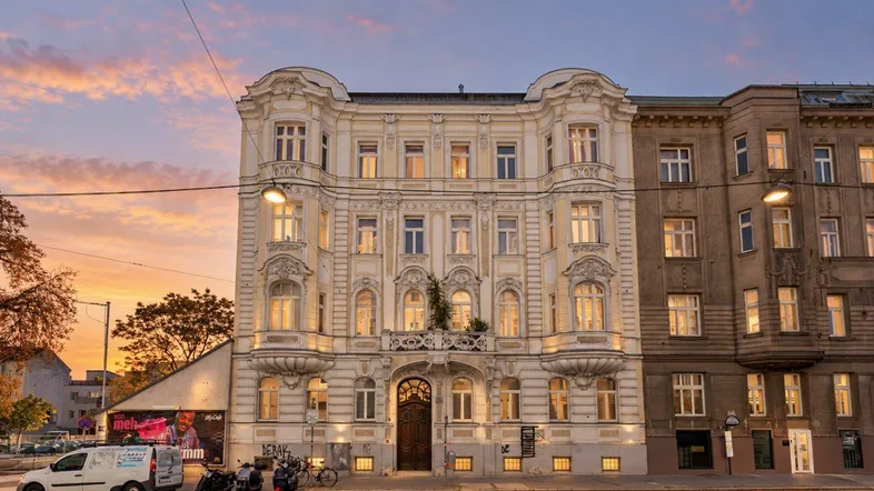 Ornates Gebäude mit historischer Fassade bei Sonnenuntergang, beleuchtet von Straßenlaternen.