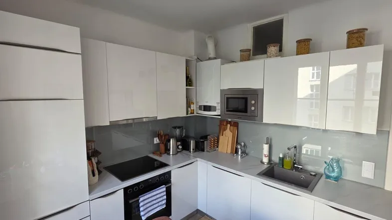 Moderne Küche mit weißen Hochglanzfronten, integrierten Geräten und einem kleinen Fenster.