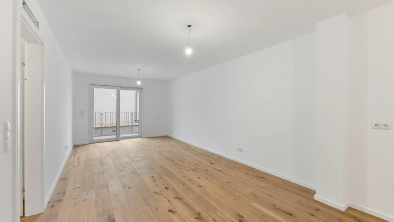 Helles, leeres Wohnzimmer mit Holzboden und Zugang zu einem französischen Balkon.