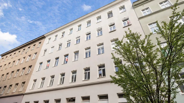 Ansicht der modernen Fassade eines Mehrfamilienhauses unter blauem Himmel mit einem Baum im Vordergrund.
