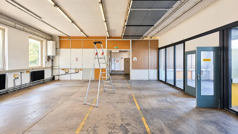 Großer, leerer Raum mit Betonboden, gelben Markierungen und Fenstern, ideal für gewerbliche Nutzung.