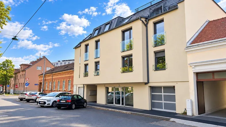 Modernes Mehrfamilienhaus mit beiger Fassade, Glasbalkonen und Dachterrasse in städtischer Umgebung.