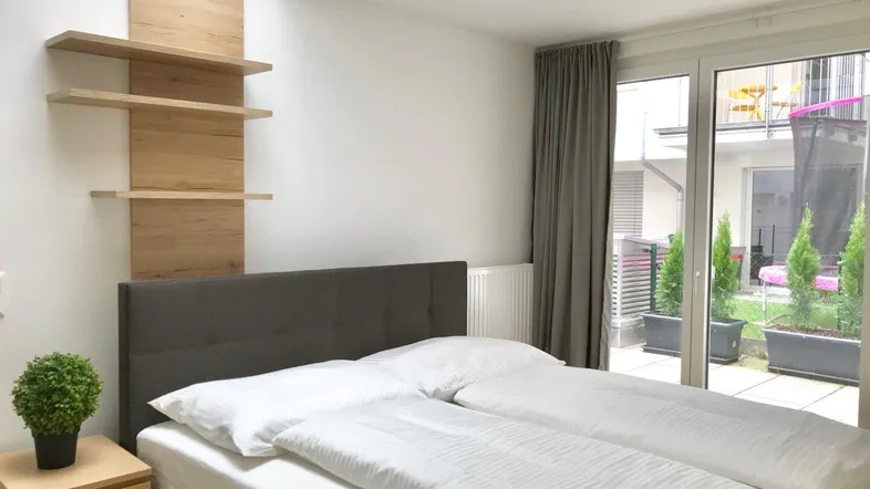 Helles Schlafzimmer mit modernem Bett, Holzregalen und Zugang zu einer kleinen Terrasse.