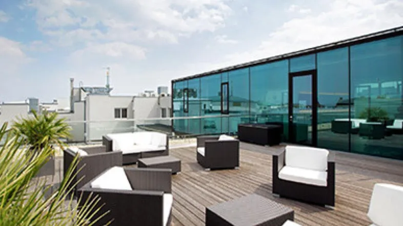 Große Dachterrasse mit bequemen Lounge-Möbeln und Blick auf eine moderne Glasfassade.