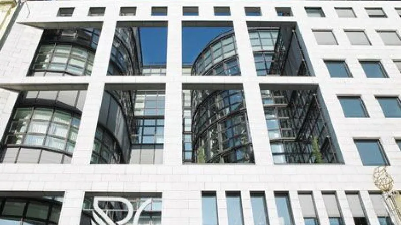 Moderne Bürogebäude-Fassade mit großen, quadratischen Fensteröffnungen und reflektierenden Glasflächen unter blauem Himmel.