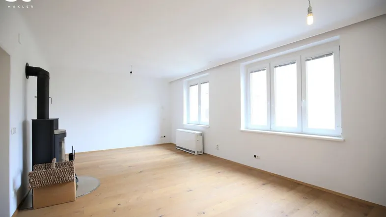 Helles Wohnzimmer mit Holzboden, Kaminofen und großen Fenstern.