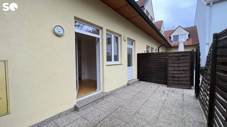 Gepflasterte Terrasse vor dem Gebäude mit Zugang zu den Innenräumen und einem Sichtschutzzaun.