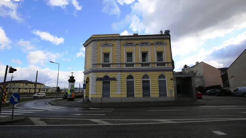 Klassisches gelbes Gebäude an einer Straßenecke mit Verzierungen und Balkonen unter bewölktem Himmel.