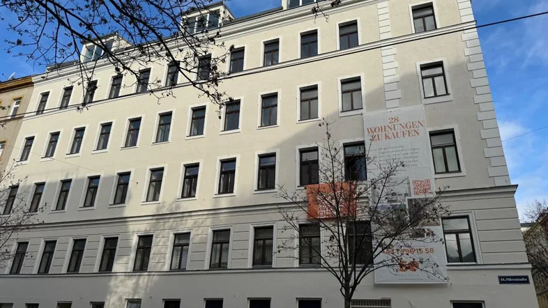 Modernisiertes Mehrfamilienhaus mit heller Fassade und großen Fenstern in städtischer Umgebung.