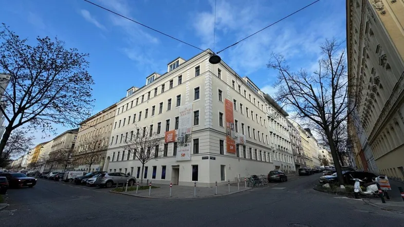 Weitwinkelaufnahme eines großen Wohngebäudes an einer Straßenecke unter blauem Himmel.