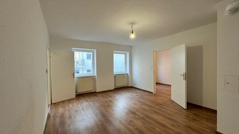 Helles Zimmer mit Laminatboden und weißen Wänden, bereit zur individuellen Gestaltung.