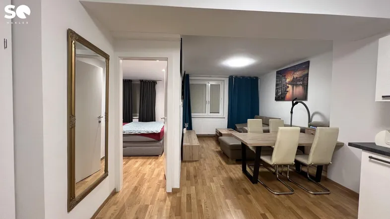 Heller Wohn- und Essbereich mit Holzboden und Blick in ein angrenzendes Schlafzimmer.