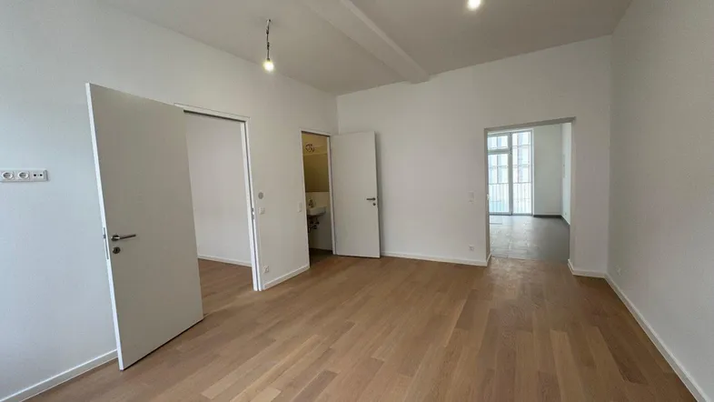 Helles, leeres Zimmer mit Holzboden und mehreren Türen, das vielseitig genutzt werden kann.
