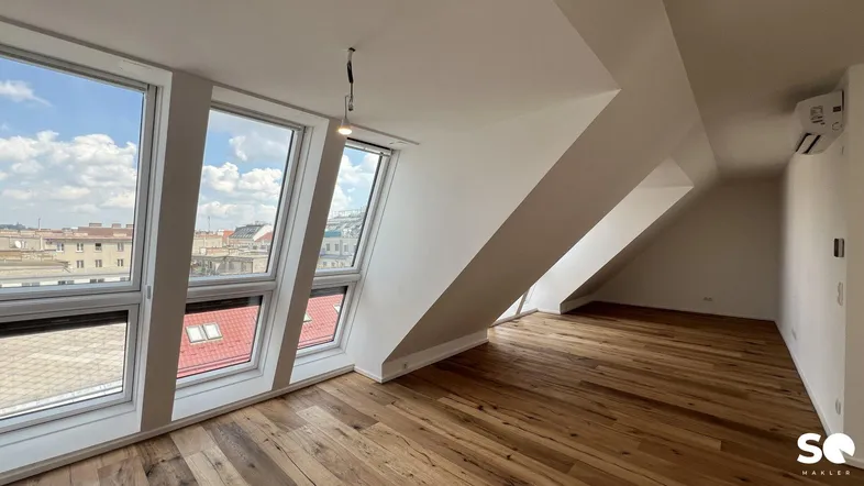 Helles Dachgeschosszimmer mit Holzboden, schrägen Wänden und großen Fenstern mit Stadtblick.