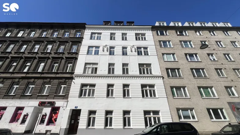 Historische Fassade eines Altbaus mit weiß gestrichener Front und angrenzenden Gebäuden in der Stadt.