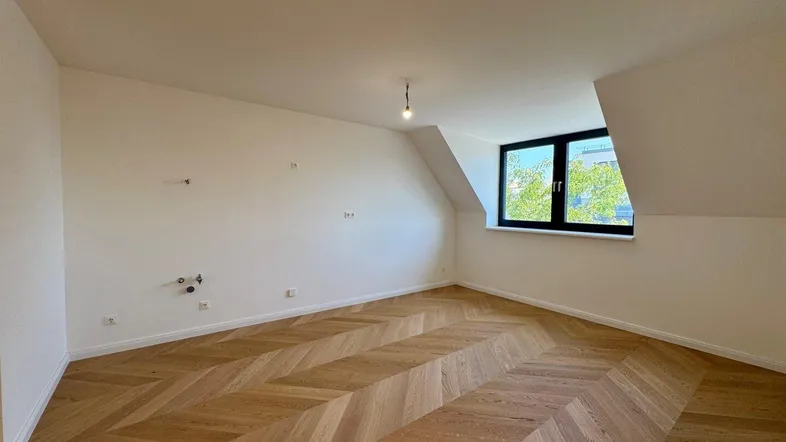 Heller Raum im Dachgeschoss mit schrägem Dach und modernem Fischgrätparkettboden.
