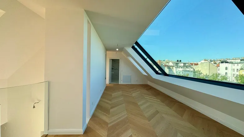 Heller Dachgeschossraum mit Fischgrätparkett und großer Dachschräge mit Fensterfront.
