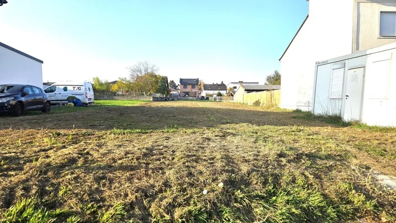 Weitläufiges unbebautes Grundstück mit trockenem Gras und umliegenden Gebäuden unter blauem Himmel.
