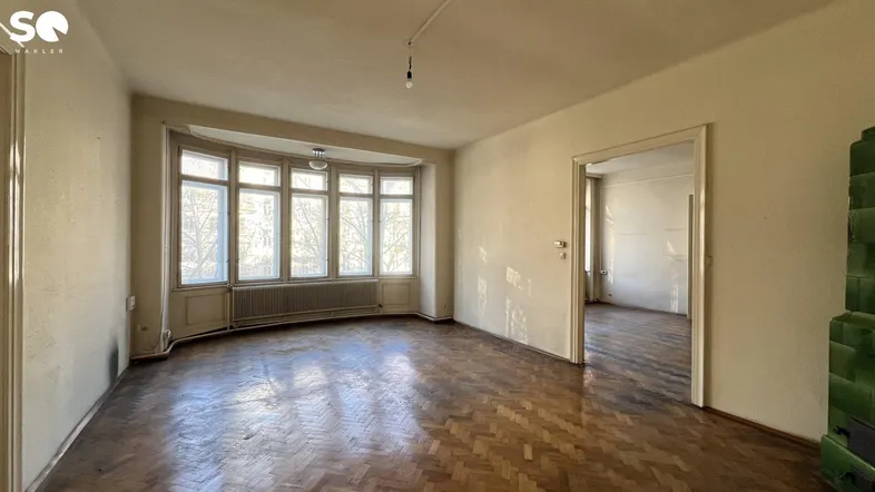 Geräumiges Wohnzimmer mit Fischgrätparkett, Erkerfenstern und viel Tageslicht, bereit zur Renovierung.