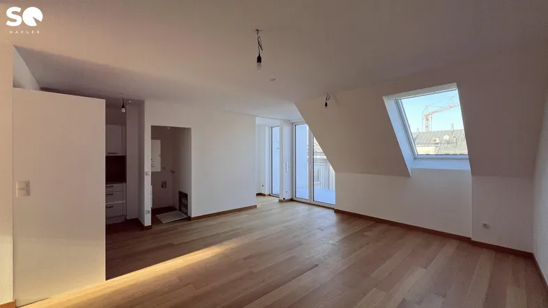 Helles Wohnzimmer mit Holzboden, Dachschrägen und Zugang zu einem Balkon, ideal für offenes Wohnen.