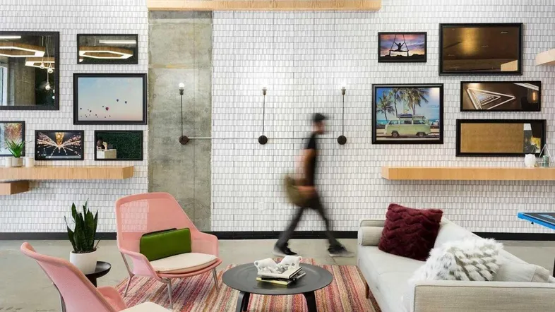 Moderner Büroloungebereich mit bequemen Sitzgelegenheiten, Kunst an der Wand und hohen Decken.